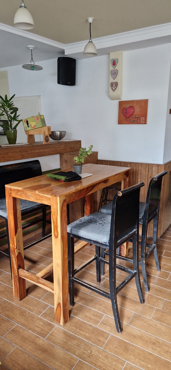 foto aus der gaststube. ein hoher tisch mit barstühlen vor der theke. ein boden mit holzoptik fliesen und es hängen bilder an der wand