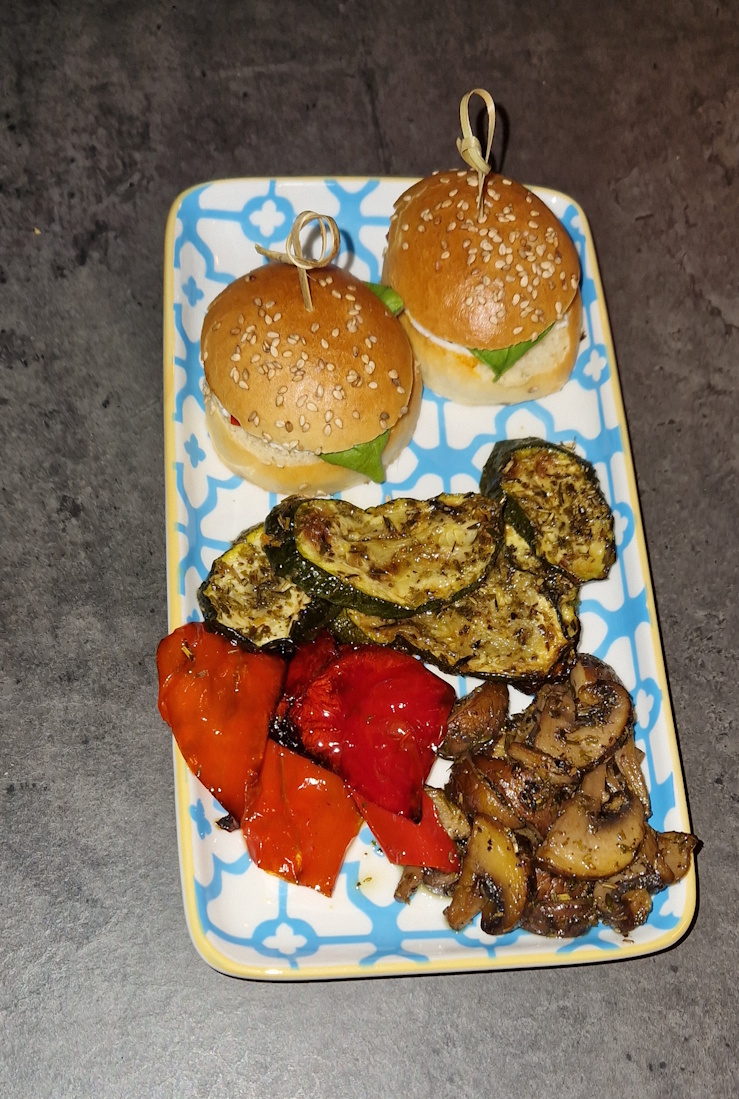 kleine vorspeisenplatte mit 2 miniburger belegt mit feta, spitzpaprika und basilikum.
                marinierte gebackene zucchini-, paprika und champignons. auf einer graumelierten thekenplatte