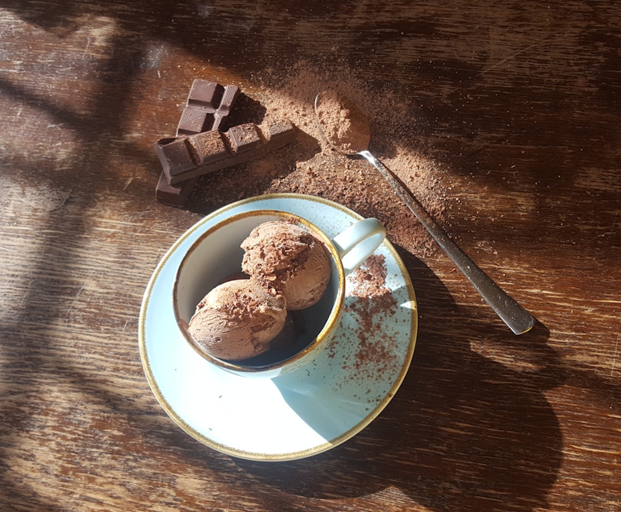 hausgemachtes schokoladeneis, in einer blaumellierten kaffeetasse auf einem alten holztisch.
                dekoriert mit fairtradekuvertüre, einem löffel mit fairen kakaopulver 